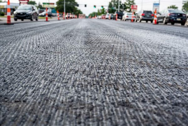 Close-up view of a new road under construction with a layer of Granular Subbase in Southern California, trucks working in the backdrop.